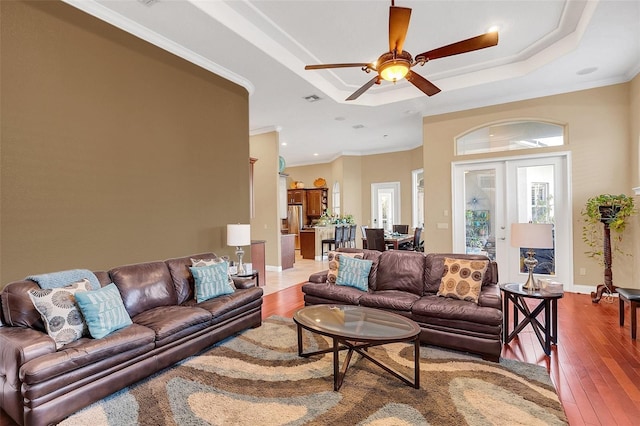 living area featuring french doors, hardwood / wood-style floors, a raised ceiling, and crown molding