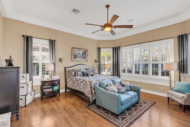 bedroom with a tray ceiling, wood finished floors, visible vents, and baseboards