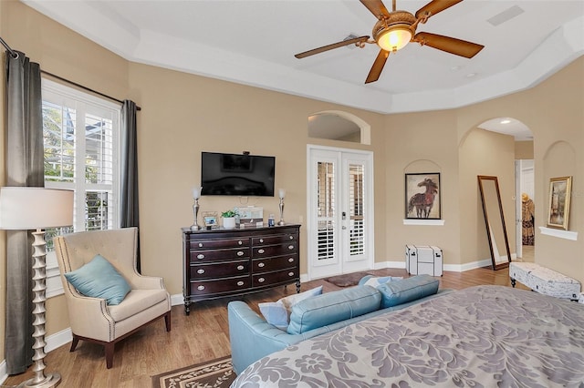 bedroom featuring arched walkways, wood finished floors, baseboards, french doors, and a tray ceiling