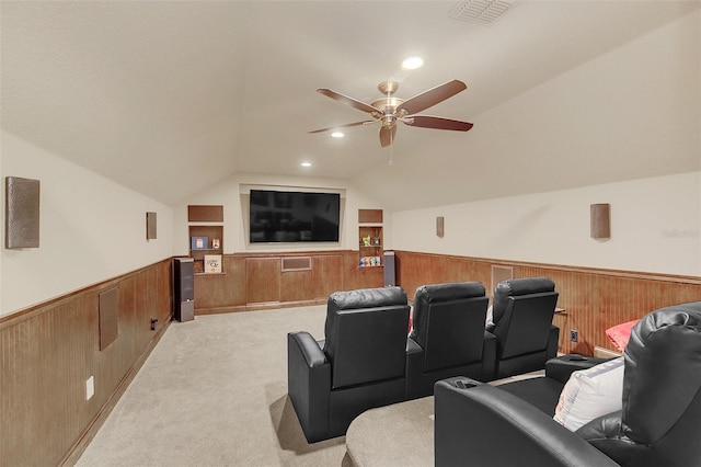 home theater room with light carpet, wooden walls, visible vents, a wainscoted wall, and vaulted ceiling