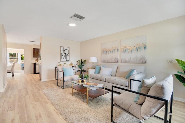 living room with light wood-style flooring, visible vents, and baseboards