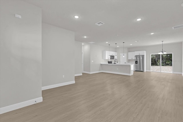 unfurnished living room with an inviting chandelier and light hardwood / wood-style floors