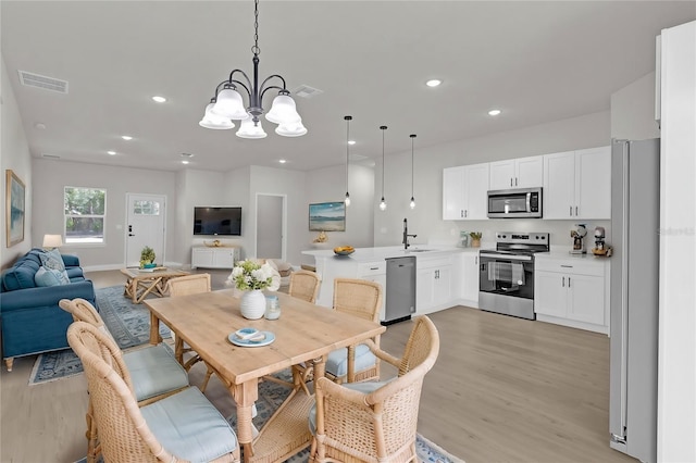 dining area with sink, a chandelier, and light wood-type flooring