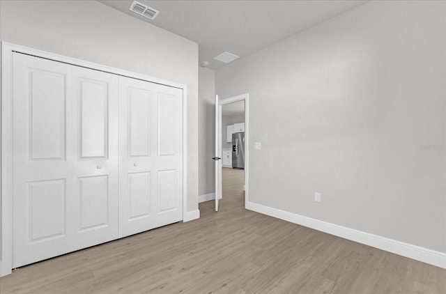 unfurnished bedroom featuring stainless steel fridge, light hardwood / wood-style floors, and a closet