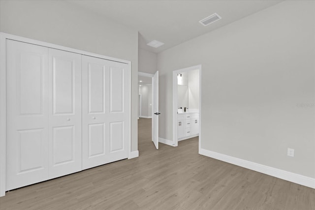 unfurnished bedroom featuring a closet, ensuite bathroom, and light hardwood / wood-style flooring