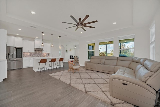 living room featuring ceiling fan, sink, a tray ceiling, and light hardwood / wood-style floors