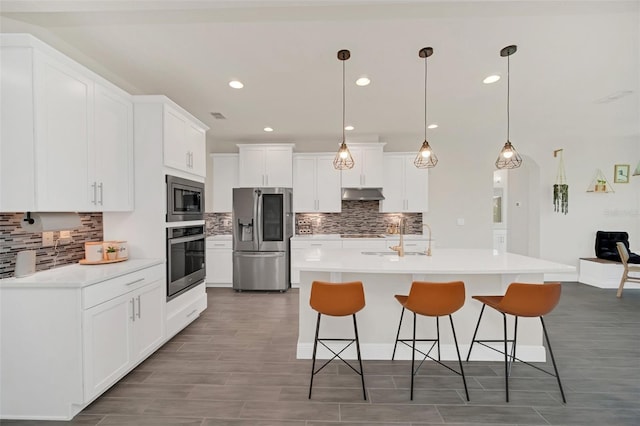 kitchen featuring an island with sink, appliances with stainless steel finishes, white cabinets, and decorative light fixtures