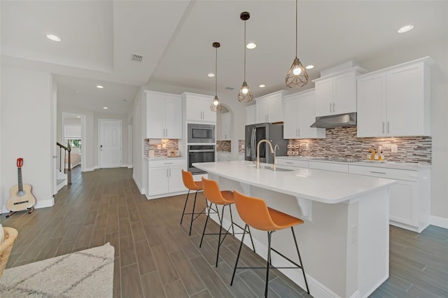 kitchen featuring a breakfast bar, decorative light fixtures, an island with sink, stainless steel appliances, and white cabinets