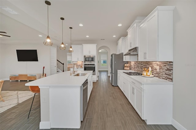 kitchen with pendant lighting, sink, appliances with stainless steel finishes, white cabinets, and a center island with sink