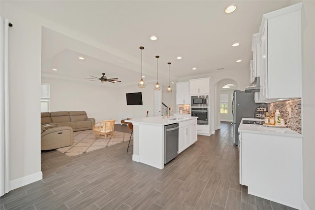 kitchen featuring pendant lighting, white cabinets, decorative backsplash, stainless steel appliances, and a center island with sink