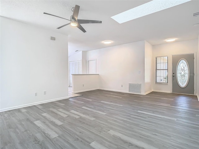 unfurnished living room with hardwood / wood-style flooring, ceiling fan, and a skylight