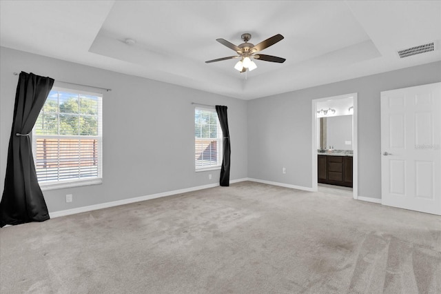 unfurnished bedroom with multiple windows, light colored carpet, and a tray ceiling