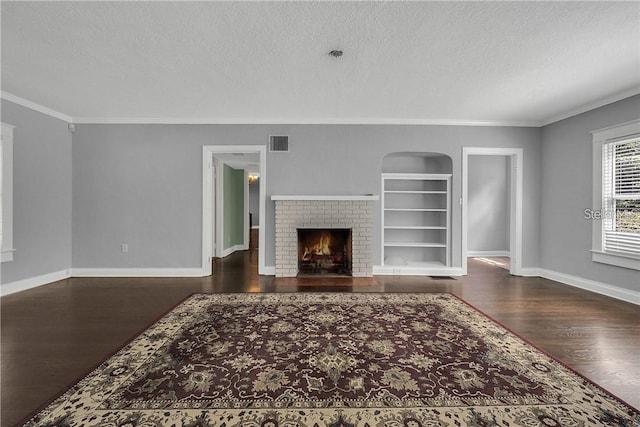 unfurnished living room featuring crown molding, dark wood-type flooring, a fireplace, a textured ceiling, and built in shelves