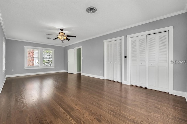 unfurnished bedroom featuring ornamental molding, dark wood-type flooring, and two closets