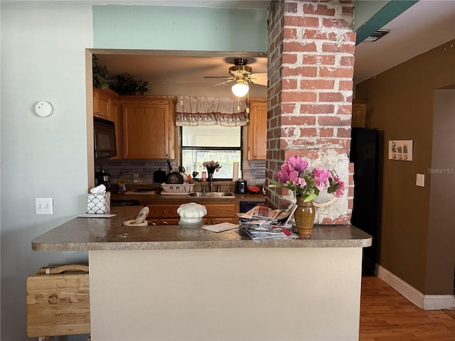 kitchen with tasteful backsplash, sink, ceiling fan, kitchen peninsula, and light hardwood / wood-style flooring