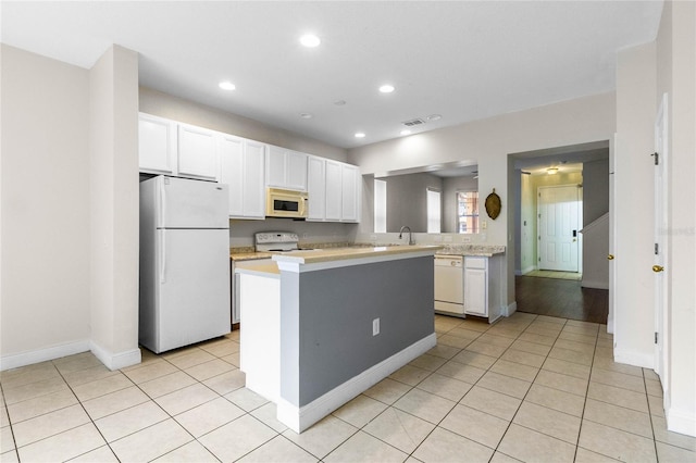 kitchen with light tile patterned floors, white cabinets, white appliances, and kitchen peninsula