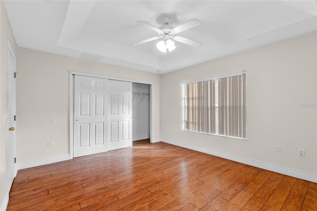 unfurnished bedroom with a tray ceiling, hardwood / wood-style flooring, a closet, and ceiling fan