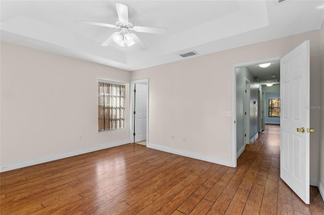 empty room featuring ceiling fan, wood-type flooring, and a tray ceiling