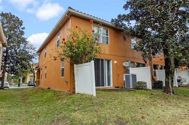 back of property with central AC unit and a lawn