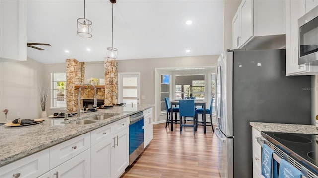 kitchen with stainless steel appliances, white cabinets, a sink, and light stone countertops