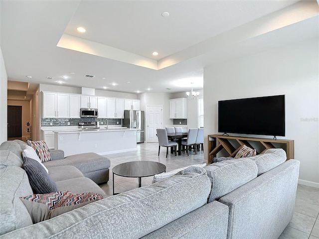 tiled living room featuring a tray ceiling, sink, and a notable chandelier