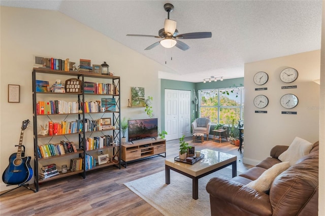 living room featuring lofted ceiling, ceiling fan, wood-type flooring, and a textured ceiling