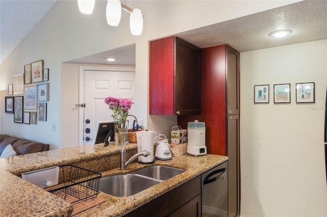 kitchen featuring pendant lighting, dishwasher, sink, light stone countertops, and a textured ceiling