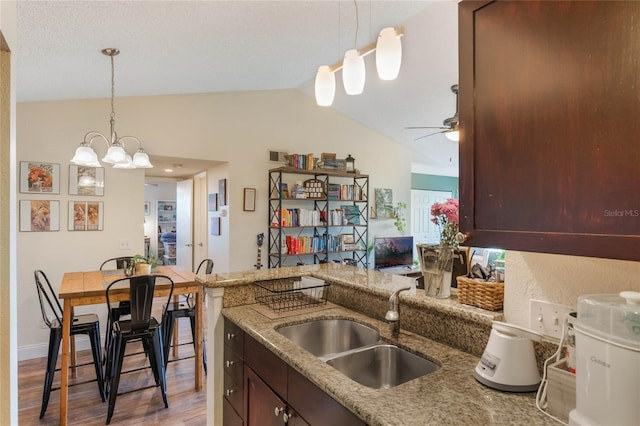 kitchen with sink, light stone counters, vaulted ceiling, hardwood / wood-style flooring, and ceiling fan with notable chandelier