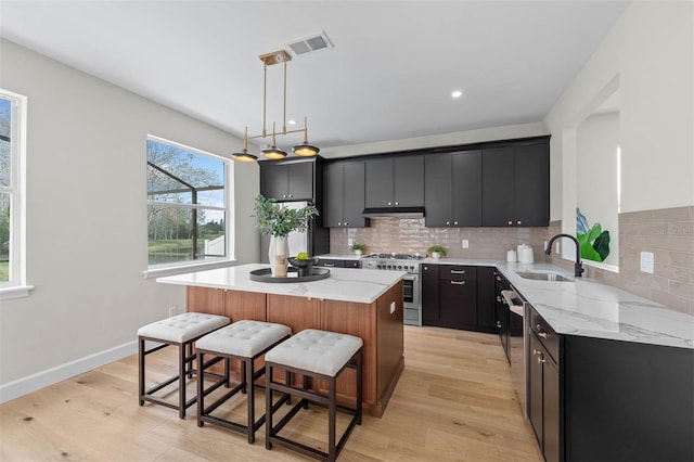 kitchen featuring light hardwood / wood-style flooring, sink, a kitchen island, decorative light fixtures, and stainless steel appliances