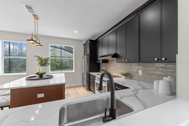 kitchen with light hardwood / wood-style flooring, light stone countertops, backsplash, and decorative light fixtures