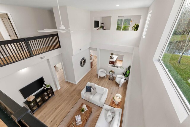 living room featuring light hardwood / wood-style floors, ceiling fan, and a high ceiling