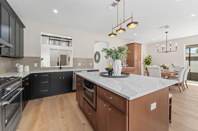 kitchen with appliances with stainless steel finishes, sink, light stone counters, a center island, and pendant lighting