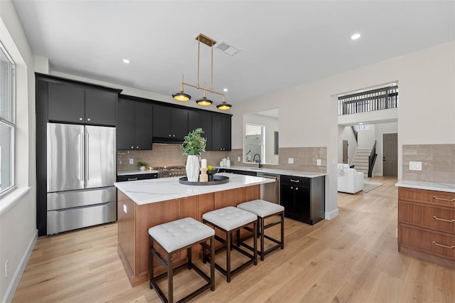 kitchen with appliances with stainless steel finishes, light hardwood / wood-style flooring, a center island, and pendant lighting