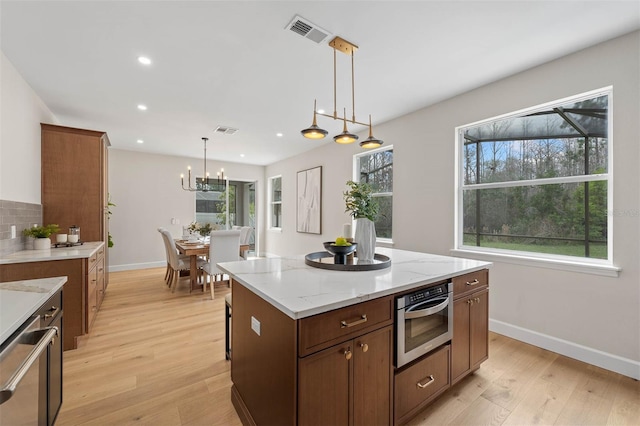 kitchen with light hardwood / wood-style flooring, hanging light fixtures, stainless steel oven, and a center island