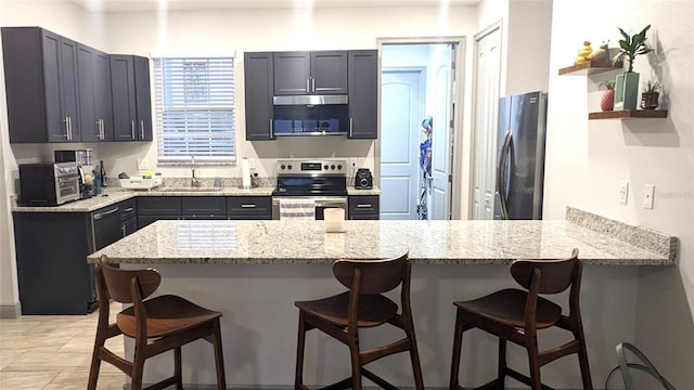 kitchen with light stone counters, sink, a breakfast bar area, and appliances with stainless steel finishes