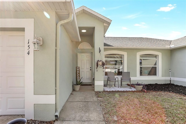 property entrance featuring a garage, roof with shingles, and stucco siding