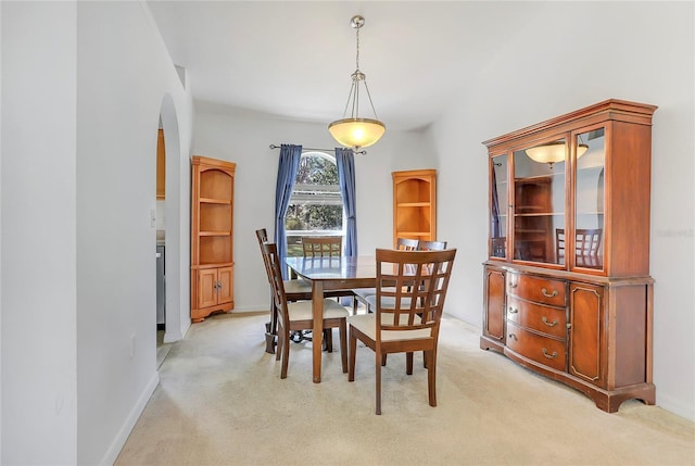 dining space featuring arched walkways, baseboards, and light colored carpet