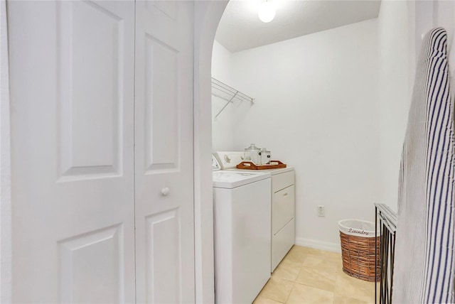 clothes washing area with laundry area, light tile patterned floors, baseboards, arched walkways, and washing machine and clothes dryer