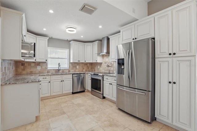 kitchen with light stone counters, visible vents, a sink, stainless steel appliances, and wall chimney exhaust hood