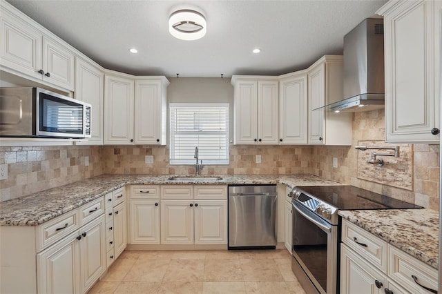 kitchen with a sink, light stone counters, stainless steel appliances, wall chimney range hood, and decorative backsplash