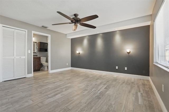 unfurnished bedroom with baseboards, light wood finished floors, ceiling fan, ensuite bathroom, and a textured ceiling