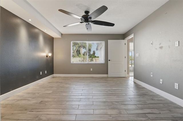 empty room with wood finished floors, baseboards, ceiling fan, a textured ceiling, and a textured wall