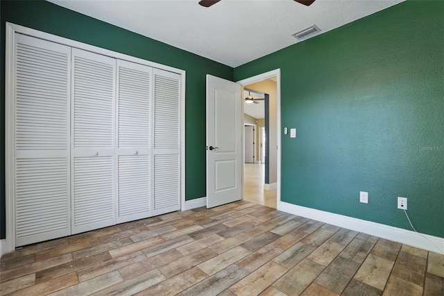 unfurnished bedroom with visible vents, baseboards, wood finished floors, a textured wall, and a closet