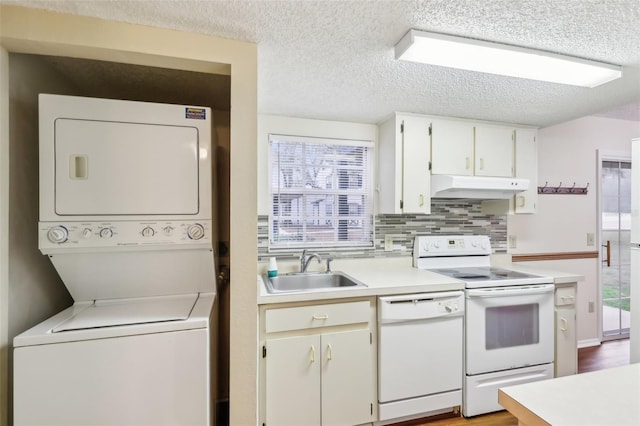 kitchen featuring white cabinetry, sink, decorative backsplash, stacked washer and dryer, and white appliances