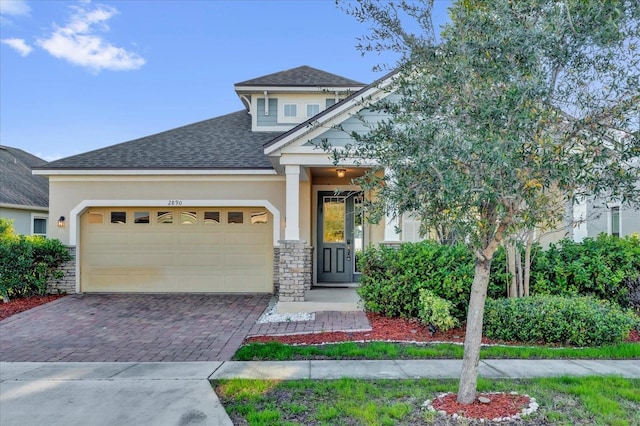 craftsman-style home featuring an attached garage, stucco siding, decorative driveway, and roof with shingles