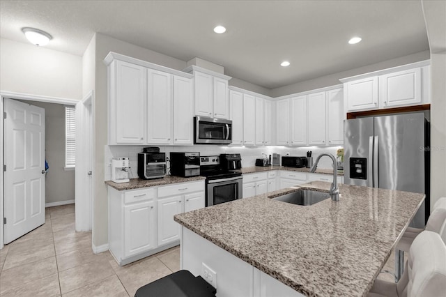 kitchen with white cabinets, light stone counters, appliances with stainless steel finishes, a kitchen island with sink, and a sink