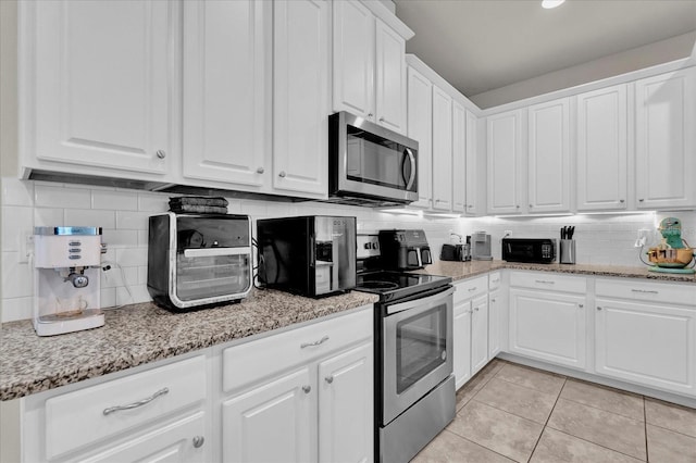 kitchen with light tile patterned floors, light stone counters, stainless steel appliances, white cabinetry, and tasteful backsplash