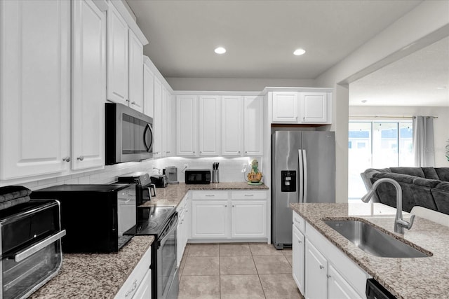 kitchen featuring tasteful backsplash, open floor plan, white cabinets, a sink, and black appliances