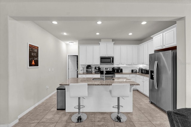 kitchen featuring appliances with stainless steel finishes, light stone countertops, a kitchen island with sink, a kitchen bar, and white cabinetry