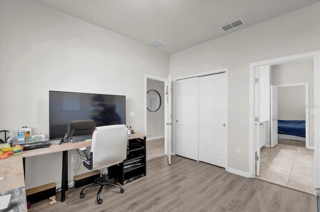 office area with light wood-type flooring, visible vents, and baseboards